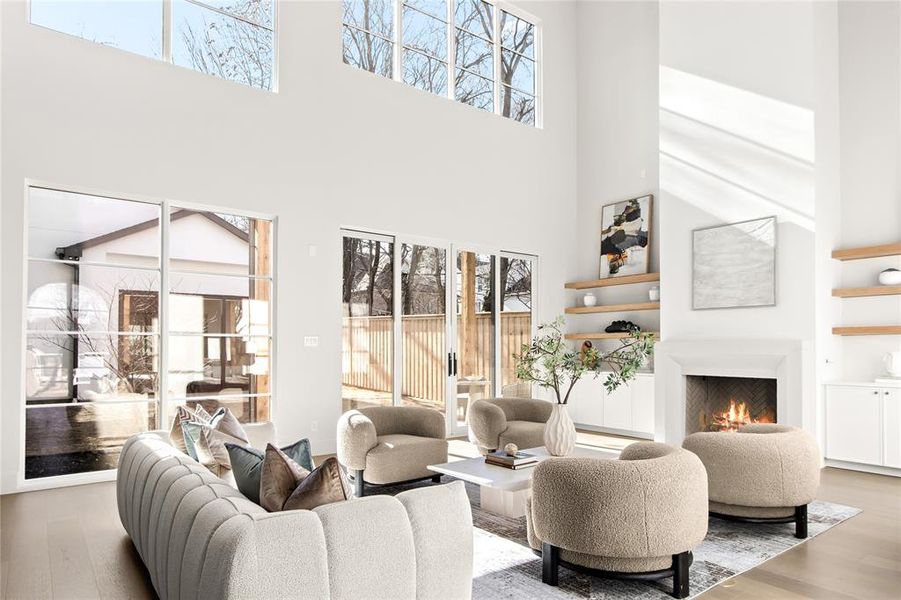 Living area featuring a two-story ceiling, multiple large windows, a fireplace with a stone surround, built-in cabinetry, and wood-finish flooring