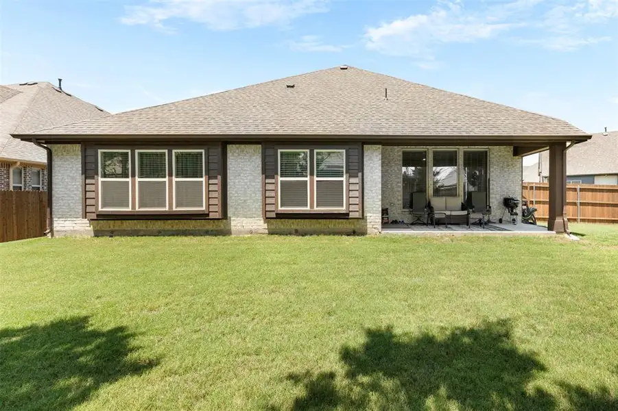 Rear exterior featuring a covered patio, expansive lawn, and partial privacy fencing Rear exterior featuring a covered patio, expansive lawn, and partial privacy fencing