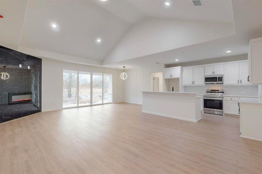 Unfurnished living room with light wood-style flooring, baseboards, high vaulted ceiling, and a premium fireplace
