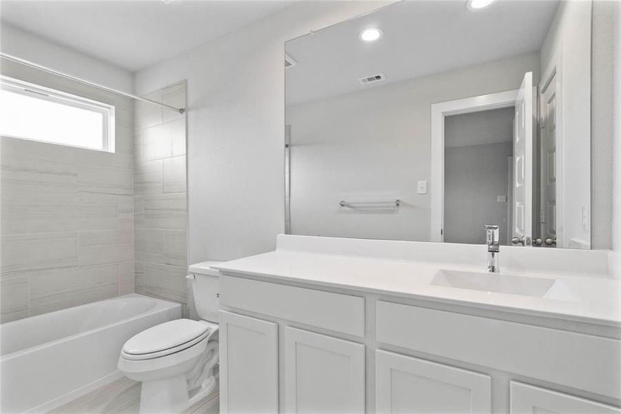 Secondary bath features tile flooring, bath/shower combo with tile surround, stained wood cabinets, beautiful light countertops, mirror, sleek fixtures and modern fini