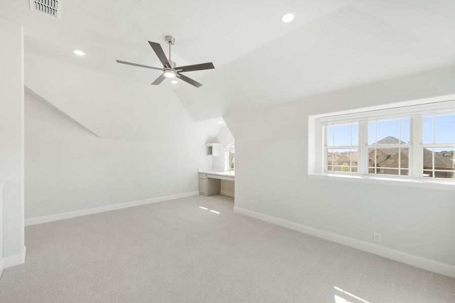 Bonus room with vaulted ceiling, ceiling fan, built-in desk, and large windows overlooking rooftops