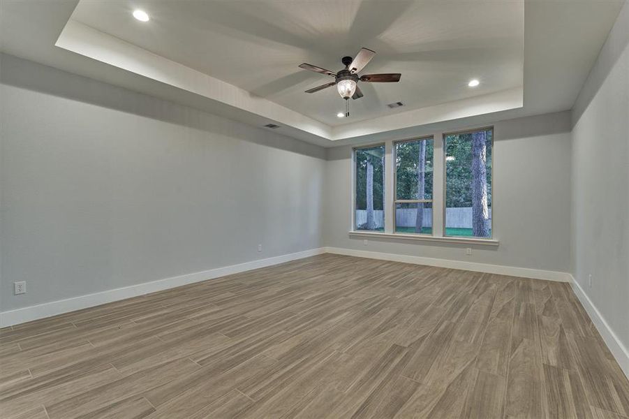 First floor primary bedroom with the easy care wood plank vinyl flooring, tray ceiling and windows overlooking the backyard.