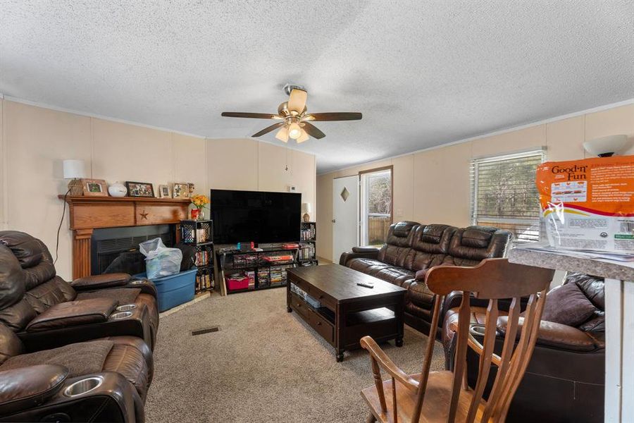 Carpeted living area featuring a textured ceiling, a fireplace, and ceiling fan Carpeted living area featuring a textured ceiling, a fireplace, and ceiling fan