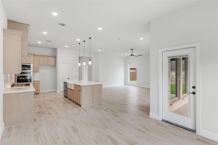 Open-concept kitchen and living area with center island, light wood cabinets, and light wood-look tile floors Open-concept kitchen and living area with center island, light wood cabinets, and light wood-look tile floors