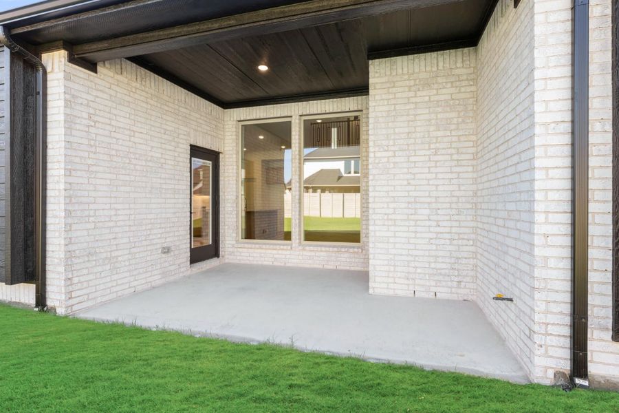 Covered back patio with concrete floor, white brick exterior, dark wood ceiling, and glass door entry