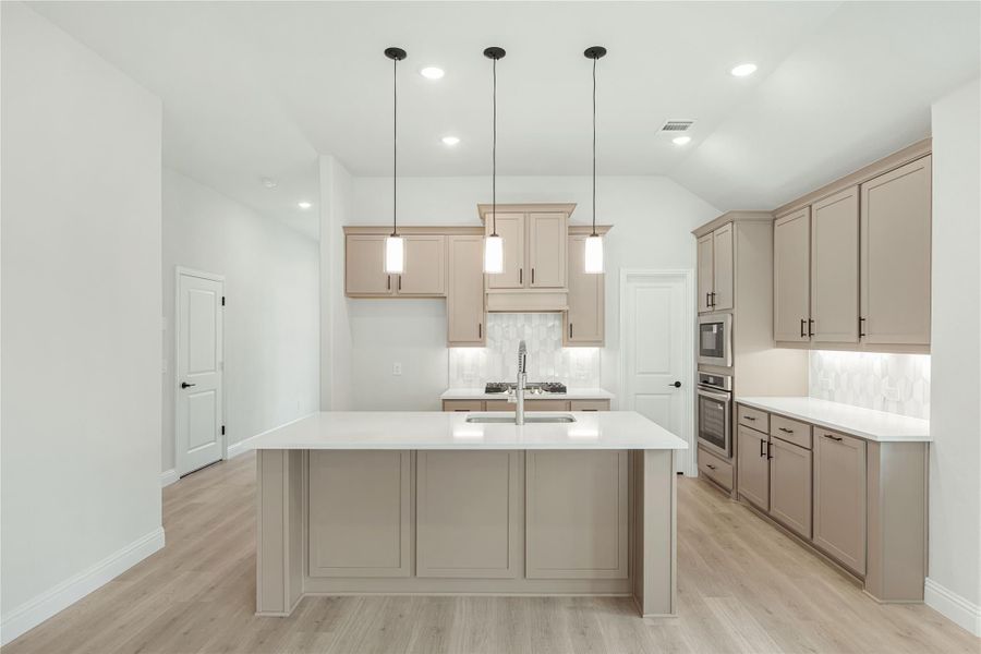 Kitchen with large center island, tan cabinets, white countertops, and three pendant lights over hardwood floors