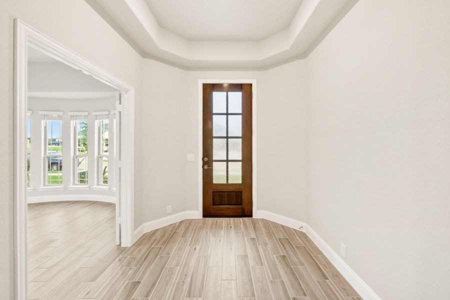 Entryway with wood front door, glass panels, tray ceiling, and light wood-look tile floors Entryway with wood front door, glass panels, tray ceiling, and light wood-look tile floors