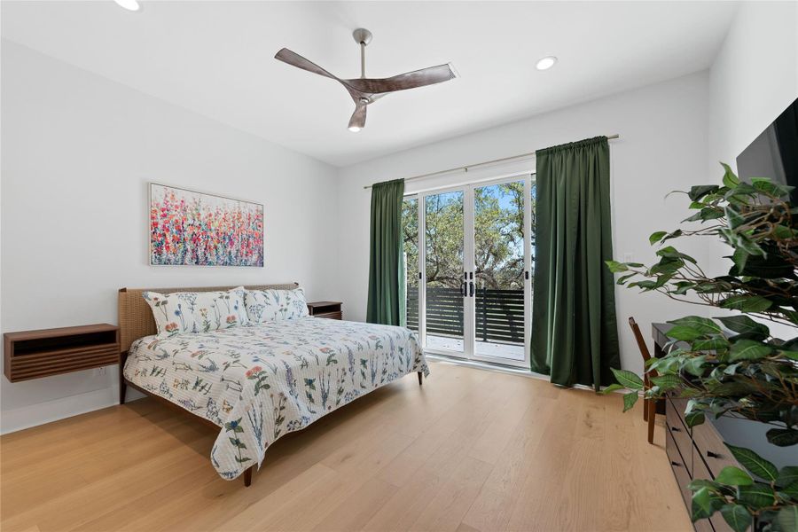 Comfortable secondary bedroom features wide-plank hardwood flooring, a modern ceiling fan, and private access to an outdoor balcony, offering guests a peaceful space with views of the surrounding mature oaks. Comfortable secondary bedroom features wide-plank hardwood flooring, a modern ceiling fan, and private access to an outdoor balcony, offering guests a peaceful space with views of the surrounding mature oaks.
