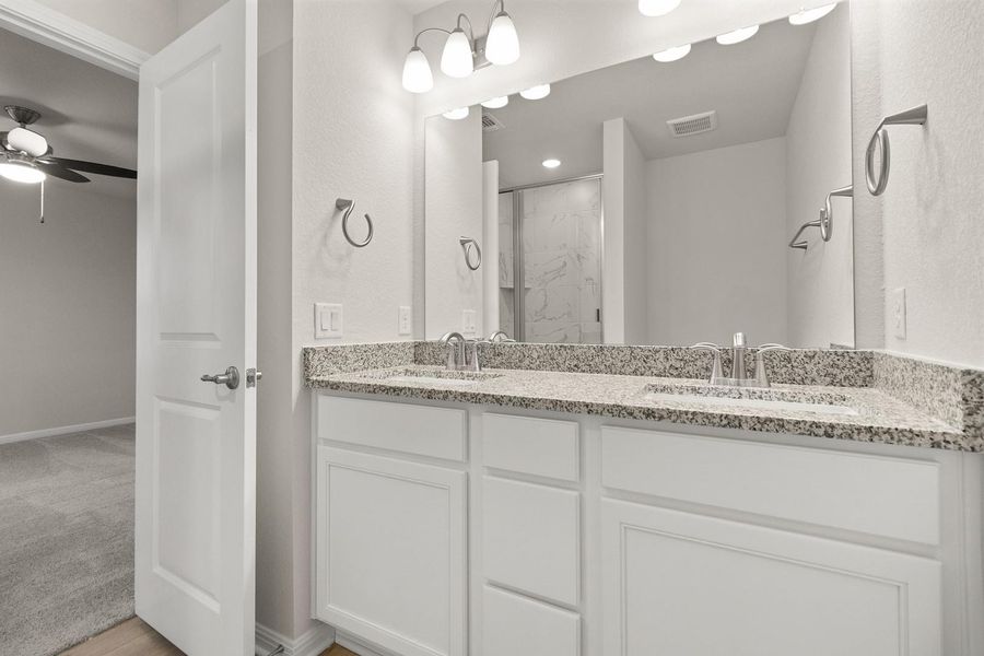Bathroom featuring a double vanity with a speckled countertop, undermount sinks, and a large mirror with overhead lighting