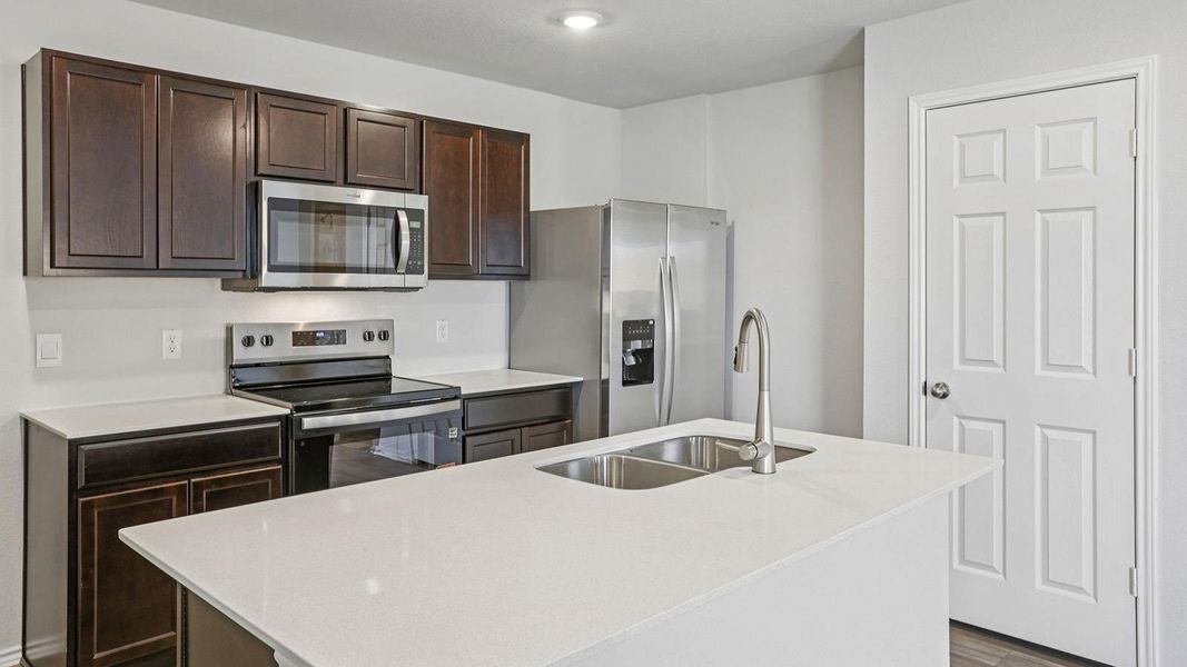 Kitchen with stainless steel appliances, dark wood finish cabinets, an island with sink, light stone counters, and dark wood-style flooring