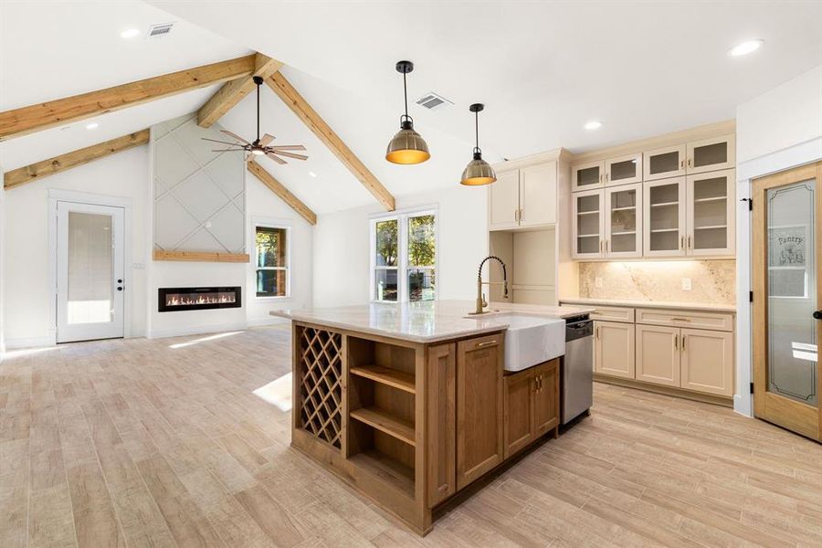 Kitchen with stainless steel dishwasher, decorative light fixtures, light wood-type flooring, and an island with sink