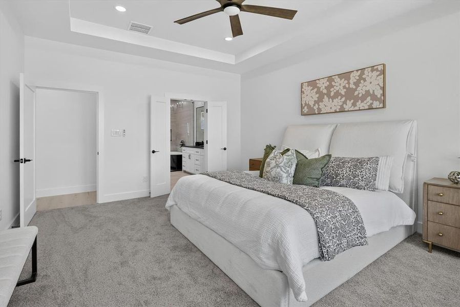 Spacious bedroom featuring light grey carpeting, white walls, a tray ceiling with recessed lighting, and a dark wood-finish ceiling fan