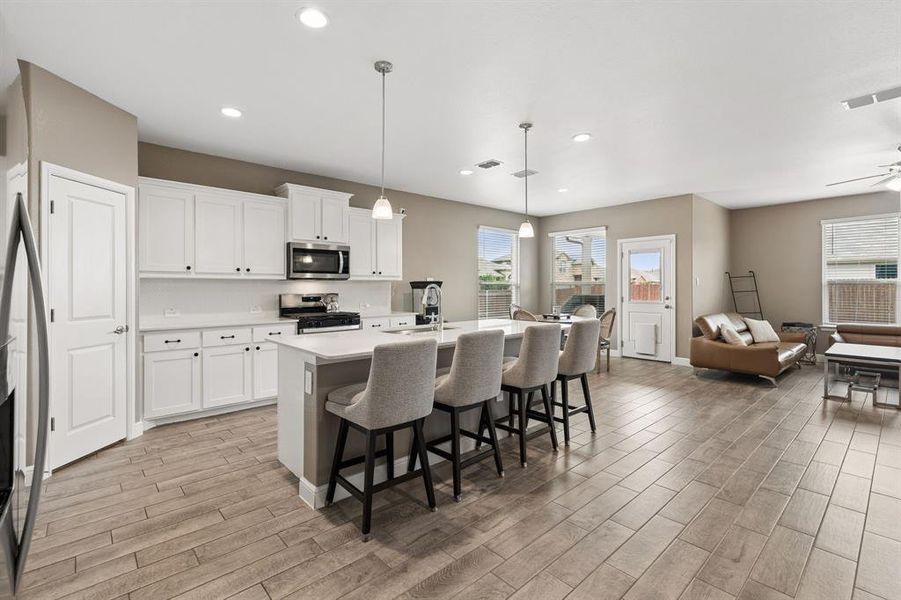 Open-concept kitchen and living area featuring wood-finish flooring, white cabinetry with dark hardware, a center island with pendant lighting, recessed lighting, and a glass-paneled exterior door