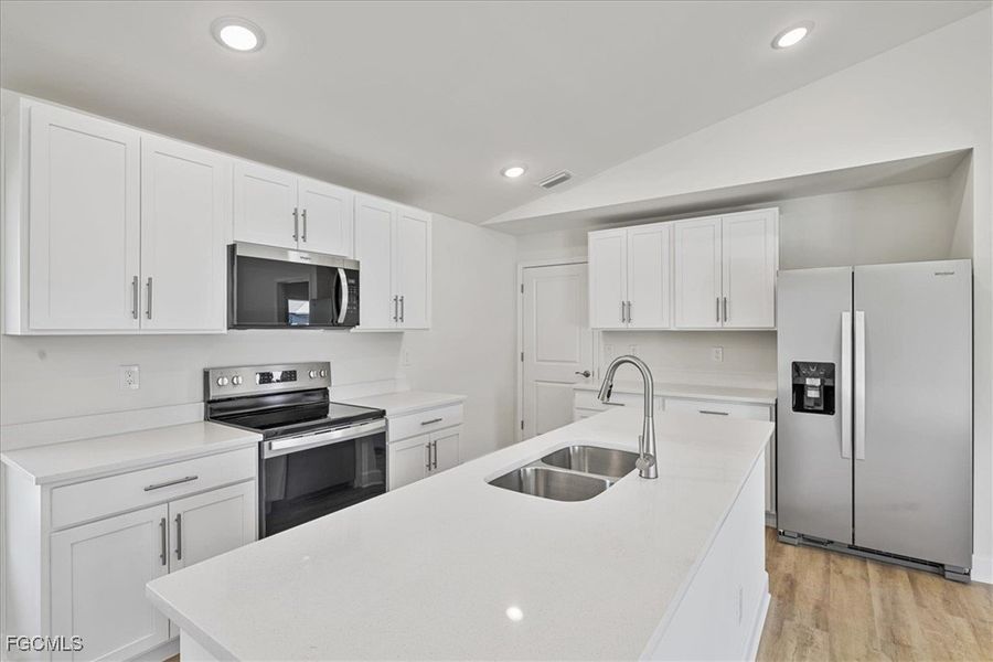 Kitchen featuring stainless steel appliances, white cabinetry, lofted ceiling, recessed lighting, and an island with sink