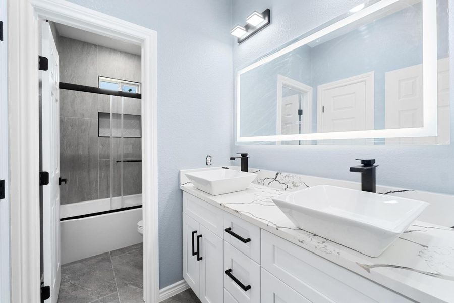 Full bath with double vanity, shower / bath combination with glass door, and a textured wall Full bath with double vanity, shower / bath combination with glass door, and a textured wall