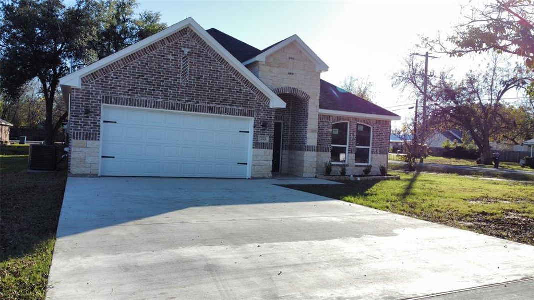 View of front of house with stone siding, a front yard, concrete driveway, and brick siding