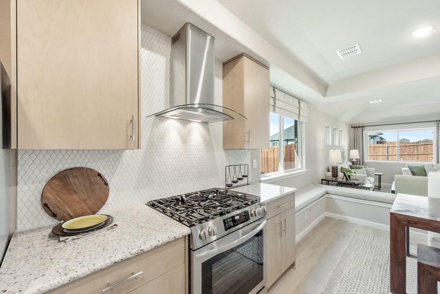 Kitchen with light wood cabinets, stainless steel gas range, and white tile backsplash open to living room Kitchen with light wood cabinets, stainless steel gas range, and white tile backsplash open to living room