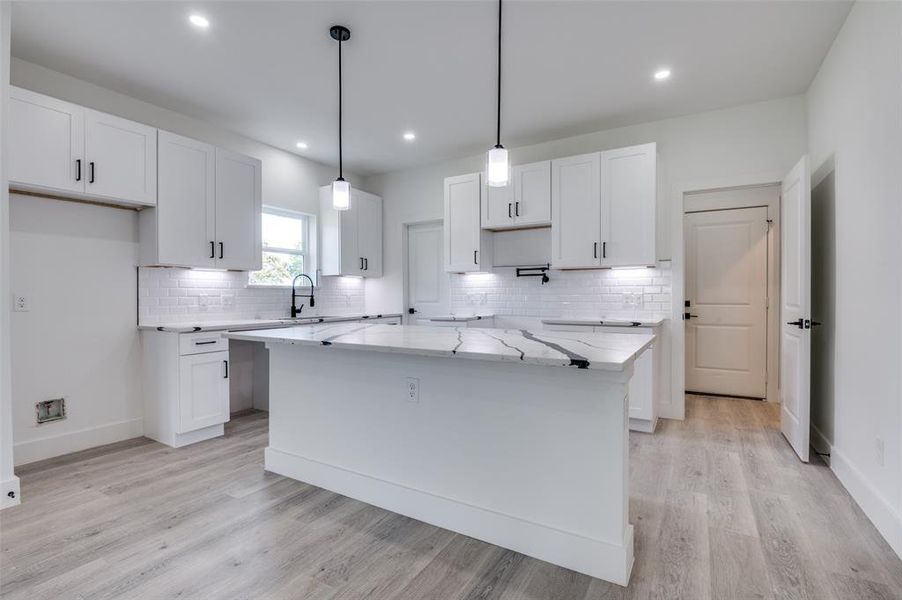 Kitchen with white cabinetry, tasteful backsplash, a center island, light wood-style flooring, and light stone counters Kitchen with white cabinetry, tasteful backsplash, a center island, light wood-style flooring, and light stone counters
