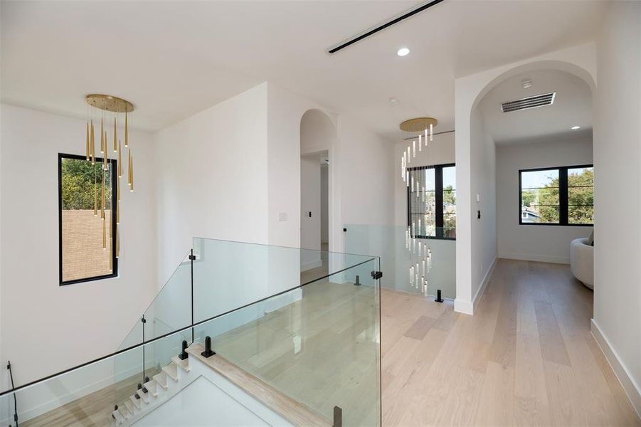 Hall with light wood-style floors, recessed lighting, arched walkways, stairs, and an upstairs landing Hall with light wood-style floors, recessed lighting, arched walkways, stairs, and an upstairs landing