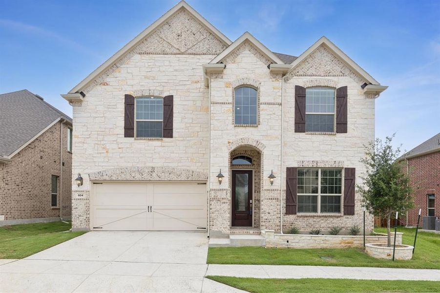 French country inspired facade with stone siding, a garage, concrete driveway, and a front yard