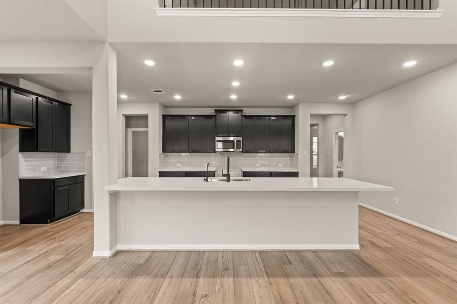 This light and bright kitchen features a large quartz island, dark stained cabinets, a large sink overlooking your family room, recessed lighting, and beautiful backsplash.