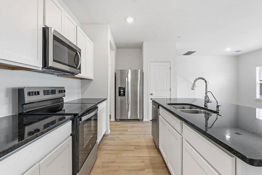 Contemporary kitchen featuring stainless steel appliances, dark countertops, white cabinetry, wood-finish flooring, and recessed lighting Contemporary kitchen featuring stainless steel appliances, dark countertops, white cabinetry, wood-finish flooring, and recessed lighting