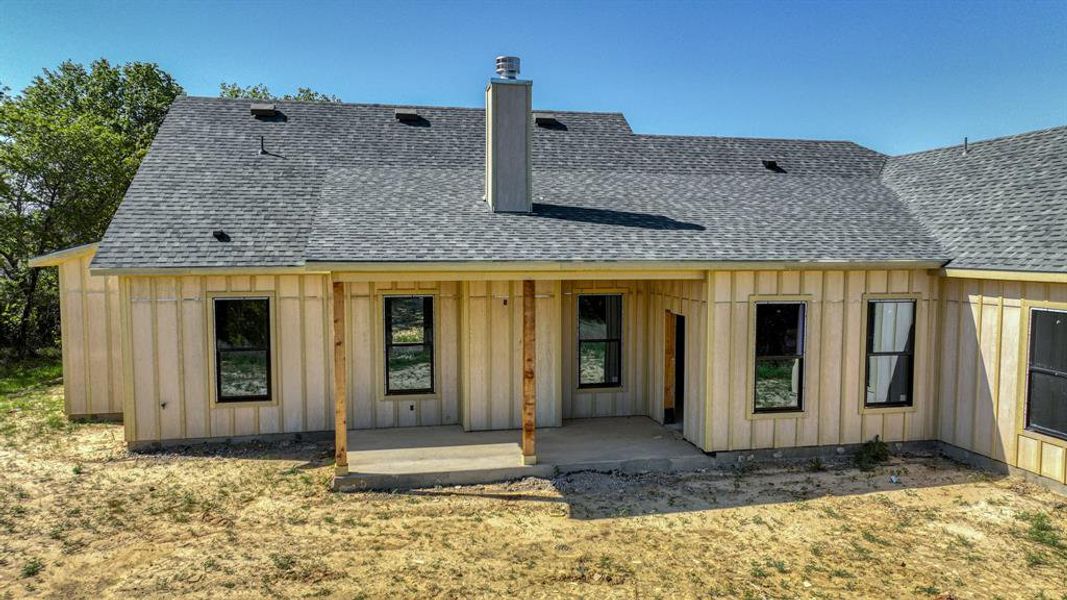 Back of house featuring a chimney, board and batten siding, a patio area, and a shingled roof Back of house featuring a chimney, board and batten siding, a patio area, and a shingled roof