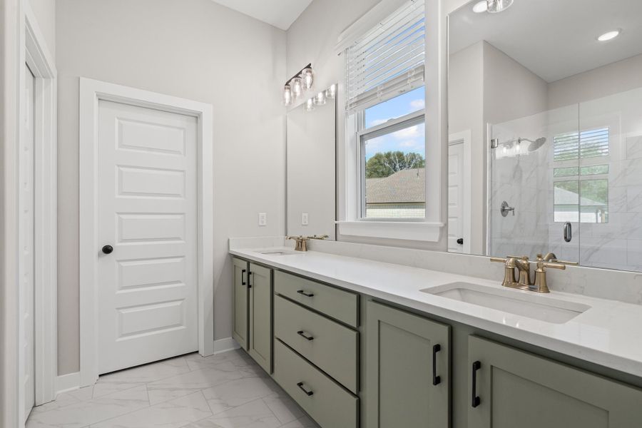 Full bathroom featuring light marble finish floors, a marble finish shower, and double vanity