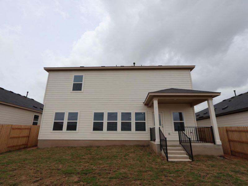 A newly constructed residence features a covered patio and a simple, fenced backyard.