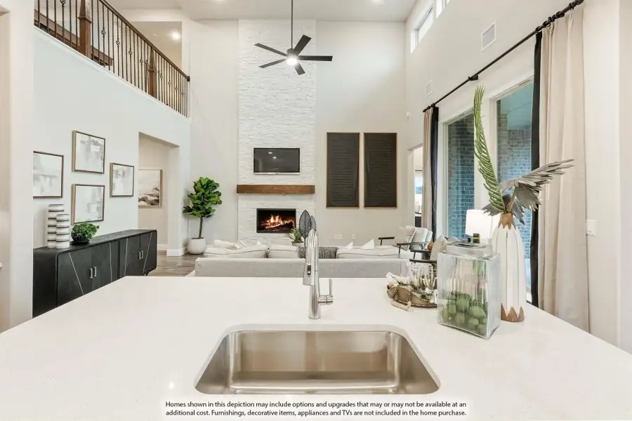 Open-concept living area with two-story ceiling, stone fireplace, and kitchen island with undermount sink in foreground.