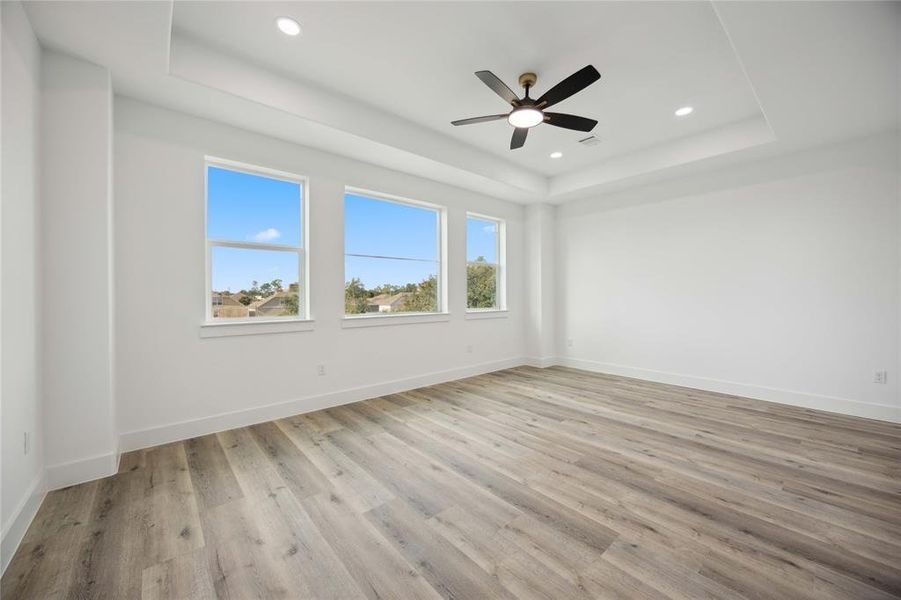 Primary bedroom on third floor offering contemporary light flooring, a modern ceiling fan, and ample natural light from three large windows. The room features a clean design with neutral finishes and recessed lighting, offering a blank canvas for personalization.