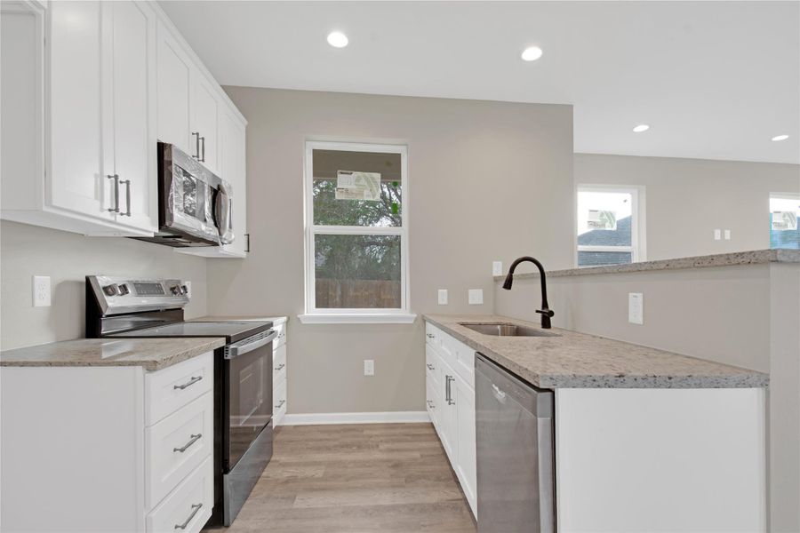 Kitchen with stainless steel appliances, light stone counters, white cabinets, healthy amount of natural light, and recessed lighting
