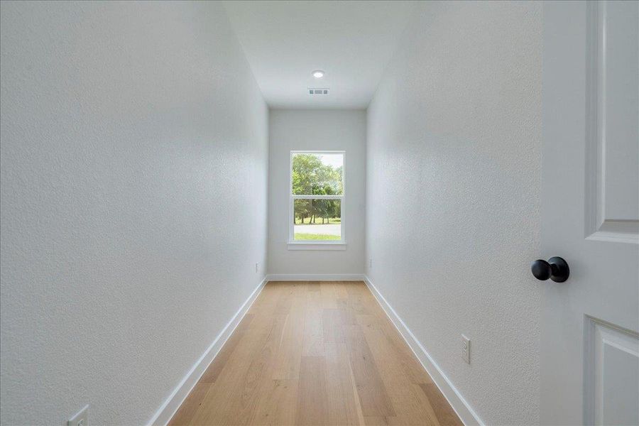 Sun-filled hallway features warm hardwood floors leading to a picturesque window overlooking lush greenery.