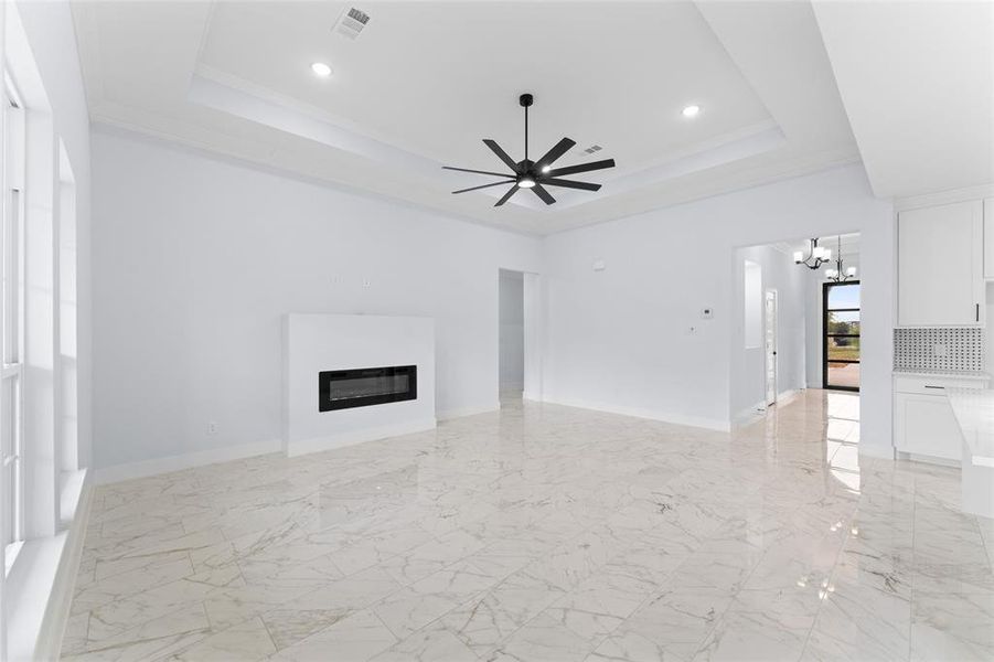 Unfurnished living room featuring crown molding, ceiling fan with notable chandelier, and a tray ceiling