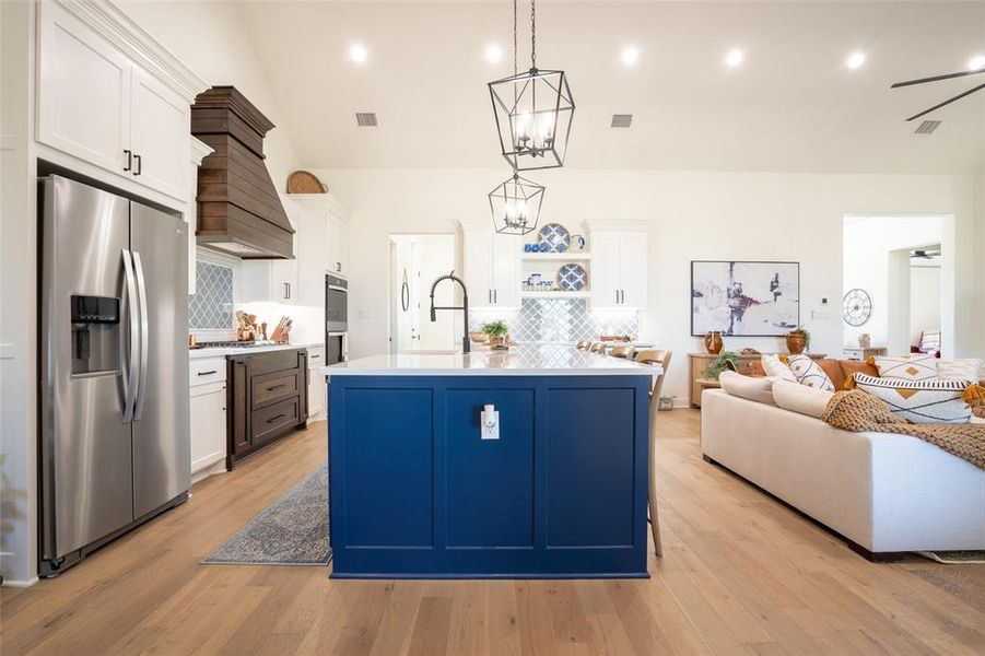 Kitchen with two tone color scheme, open floor plan, stainless steel appliances, an island with sink, and light wood-style flooring Kitchen with two tone color scheme, open floor plan, stainless steel appliances, an island with sink, and light wood-style flooring