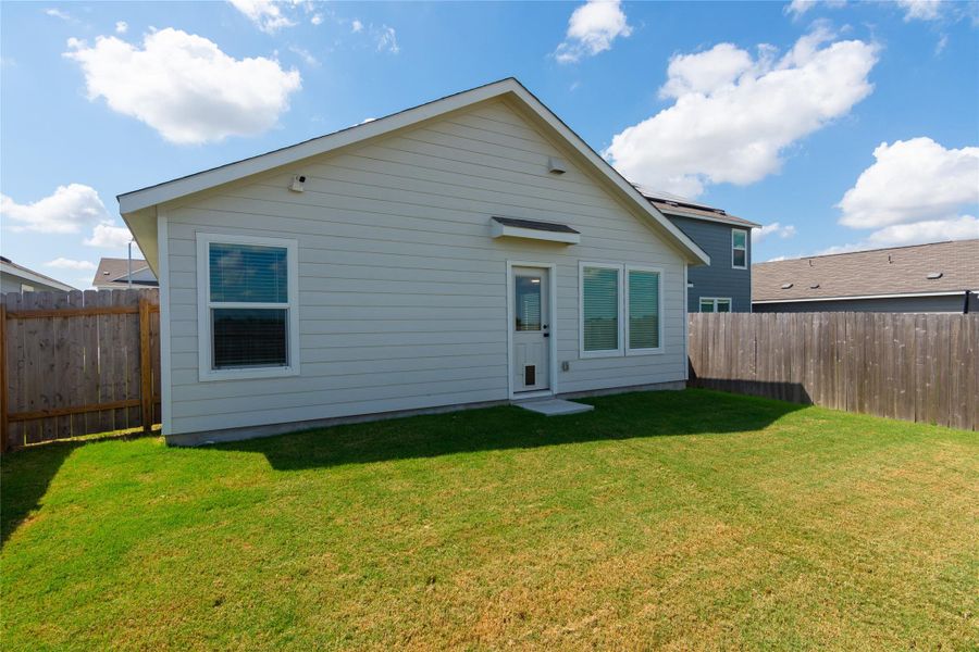 Exterior featuring siding, multiple windows, a rear entry door, and a private fenced yard with a grass lawn