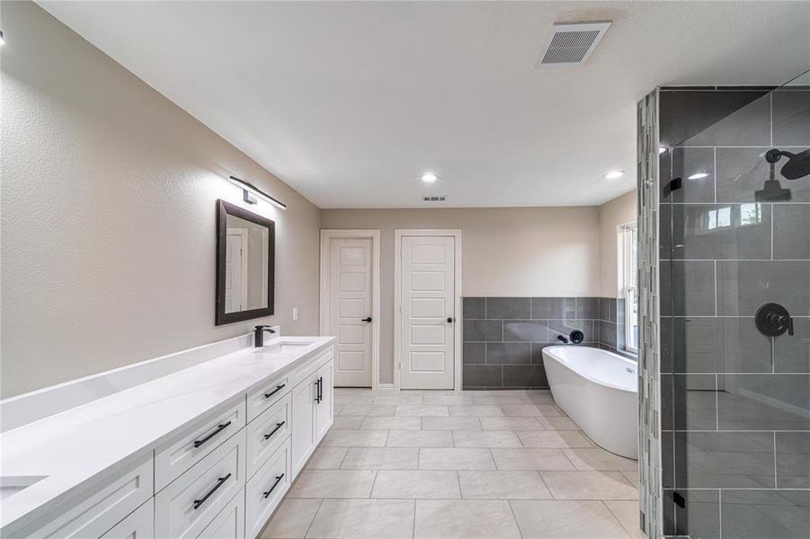 Bathroom with a stall shower, double vanity, tile walls, a freestanding tub, and a wainscoted wall