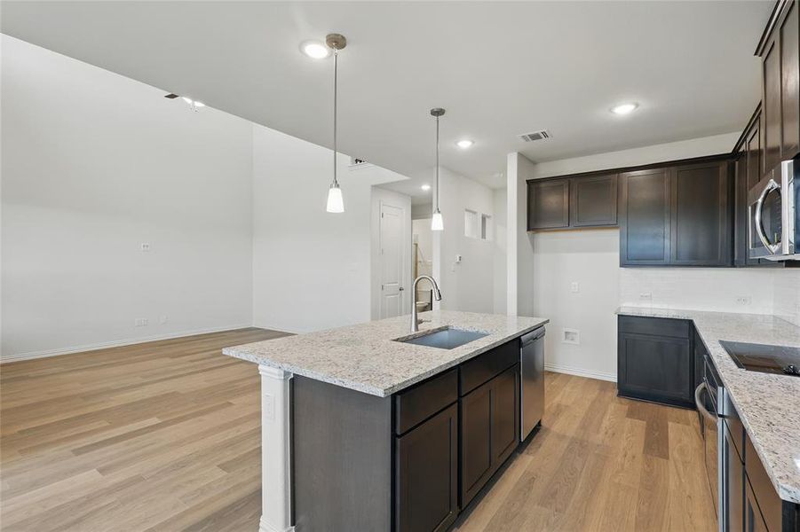 Kitchen with a sink, stainless steel appliances, light wood-style flooring, light stone counters, and dark brown cabinets Kitchen with a sink, stainless steel appliances, light wood-style flooring, light stone counters, and dark brown cabinets