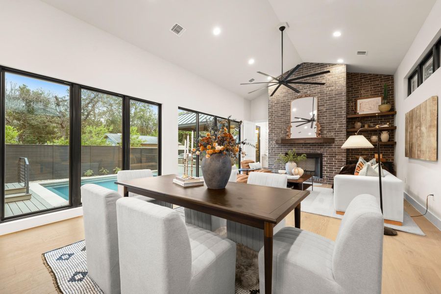 Dining area featuring a fireplace, light wood-type flooring, recessed lighting, high vaulted ceiling, and brick wall