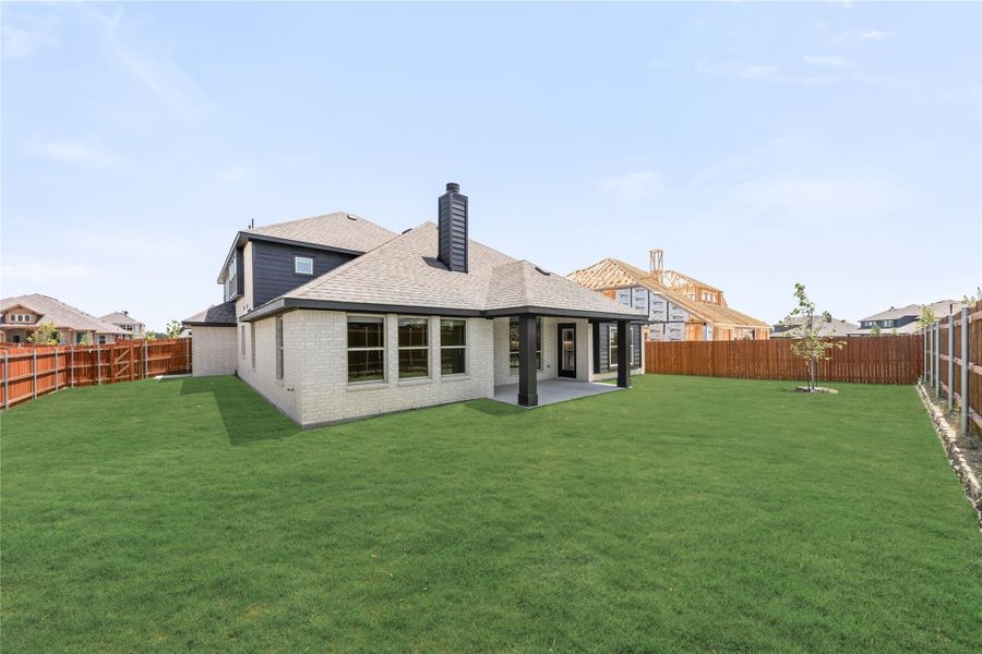 Rear view of two-story brick home with covered patio, chimney, and large fenced backyard