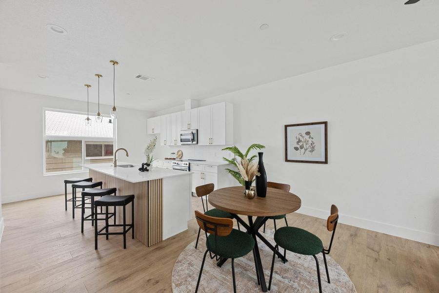 Open-concept kitchen and dining area featuring light wood-finish flooring, a kitchen island with seating, pendant lighting fixtures, white cabinetry, and stainless steel appliances