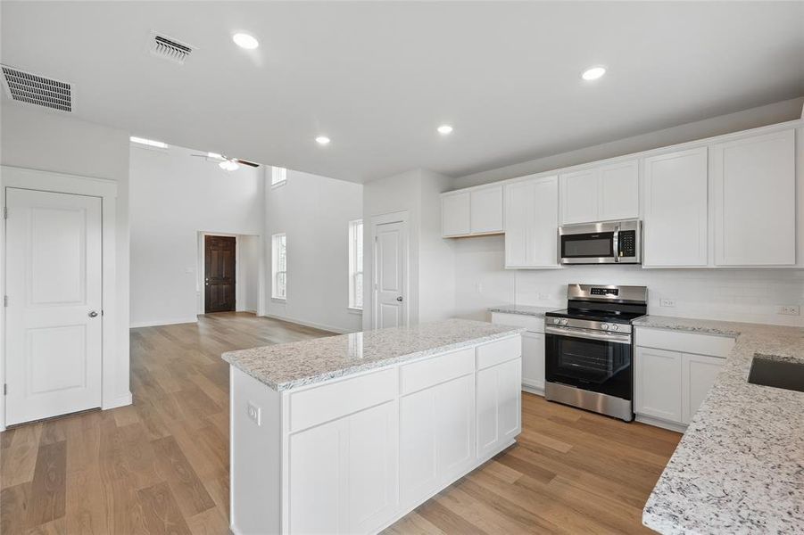 Kitchen with appliances with stainless steel finishes, a center island, light wood-style flooring, white cabinets, and recessed lighting Kitchen with appliances with stainless steel finishes, a center island, light wood-style flooring, white cabinets, and recessed lighting