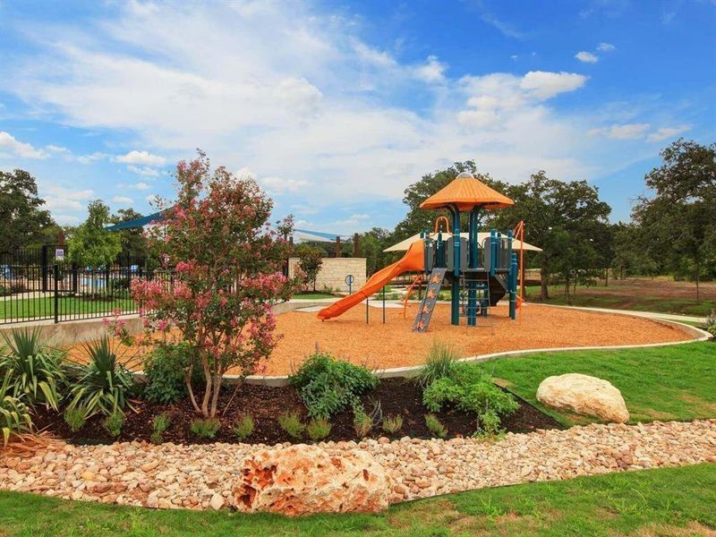 Manicured landscaping surrounds a community playground with a modern play structure under a blue sky.
