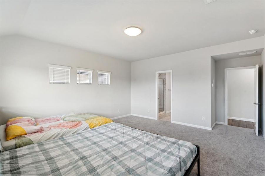 Bedroom featuring light colored carpet, vaulted ceiling, and ensuite bath