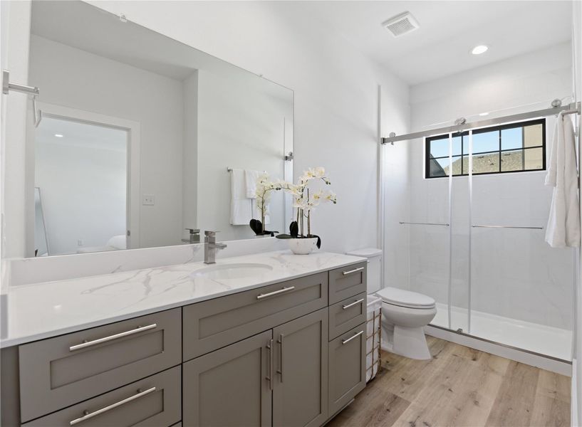 This bathroom features a modern design with a large mirror, sleek vanity with ample storage, and a spacious glass-enclosed shower.