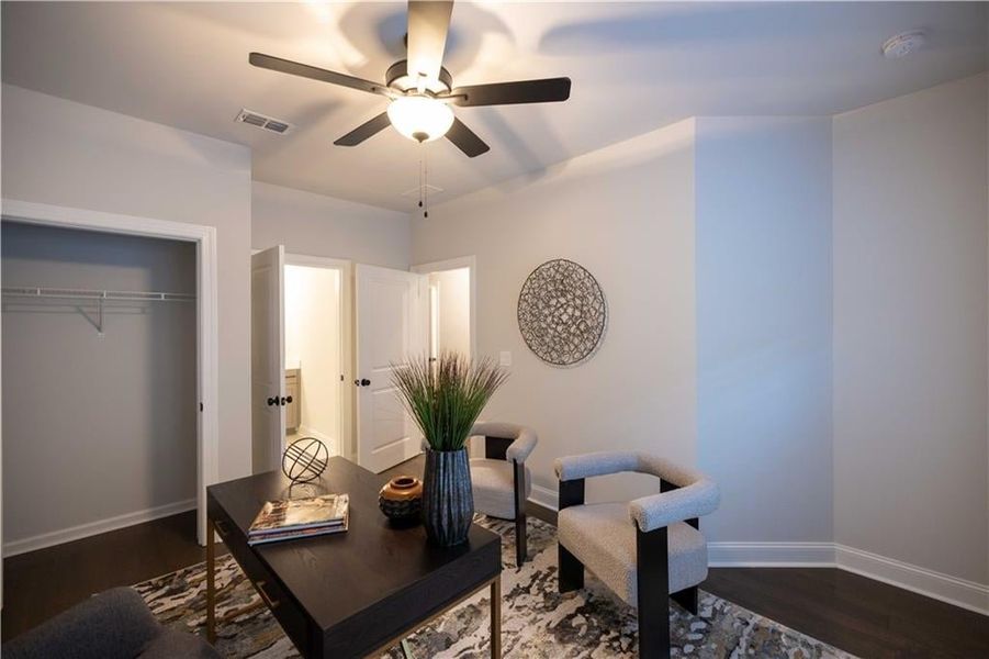 Office area with ceiling fan, dark wood-style flooring, visible vents, and baseboards