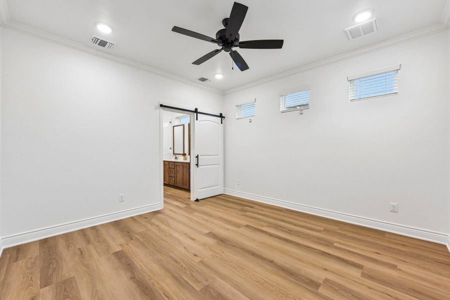 Laminate flooring extends through this naturally illuminated primary bedroom, featuring a contemporary ceiling fan and a stylish barn door leading to the ensuite. Laminate flooring extends through this naturally illuminated primary bedroom, featuring a contemporary ceiling fan and a stylish barn door leading to the ensuite.