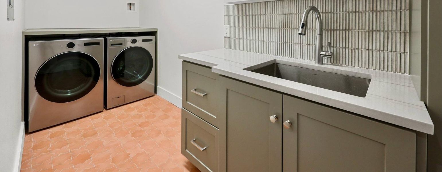 Utility room featuring a built-in sink with a gooseneck faucet, light grey cabinetry with various pulls, light-toned countertop, and a vertical tile backsplash