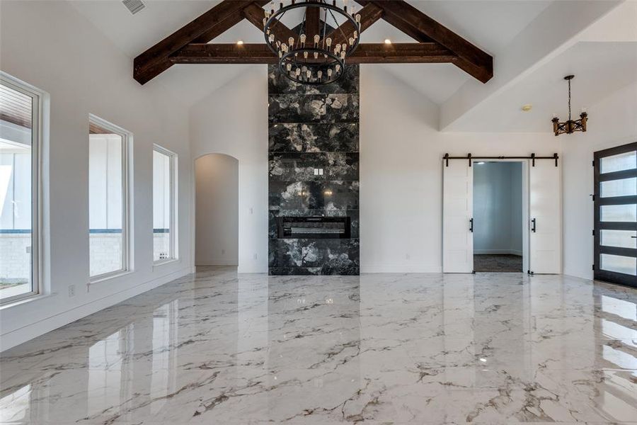 Unfurnished living room with high vaulted ceiling, beamed ceiling, plenty of natural light, and a barn door