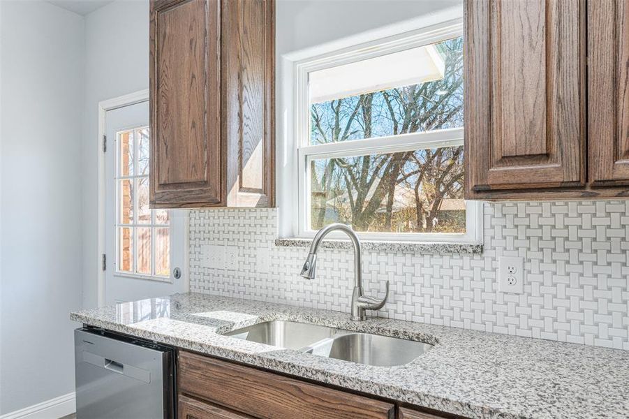 Kitchen with light stone countertops, a sink, stainless steel dishwasher, backsplash, and brown cabinets